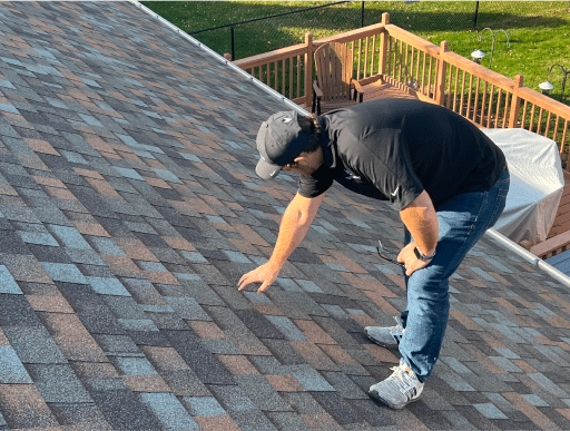 man on top of roof looking at shingles